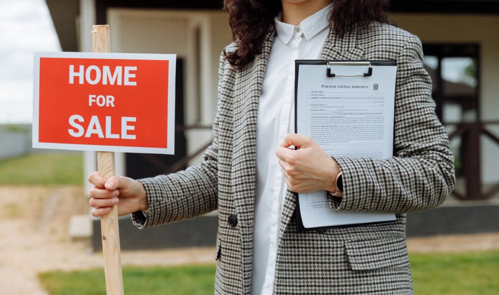 a woman holding a home-for-sale sign